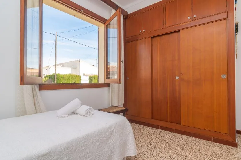 Un dormitorio con una cama junto a una ventana abierta y armarios empotrados de madera.