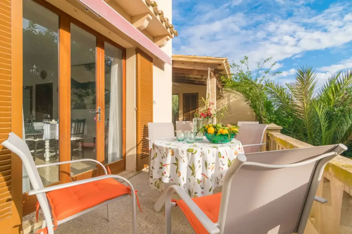 Una terraza soleada tiene asientos y una mesa puesta con platos y fruta.