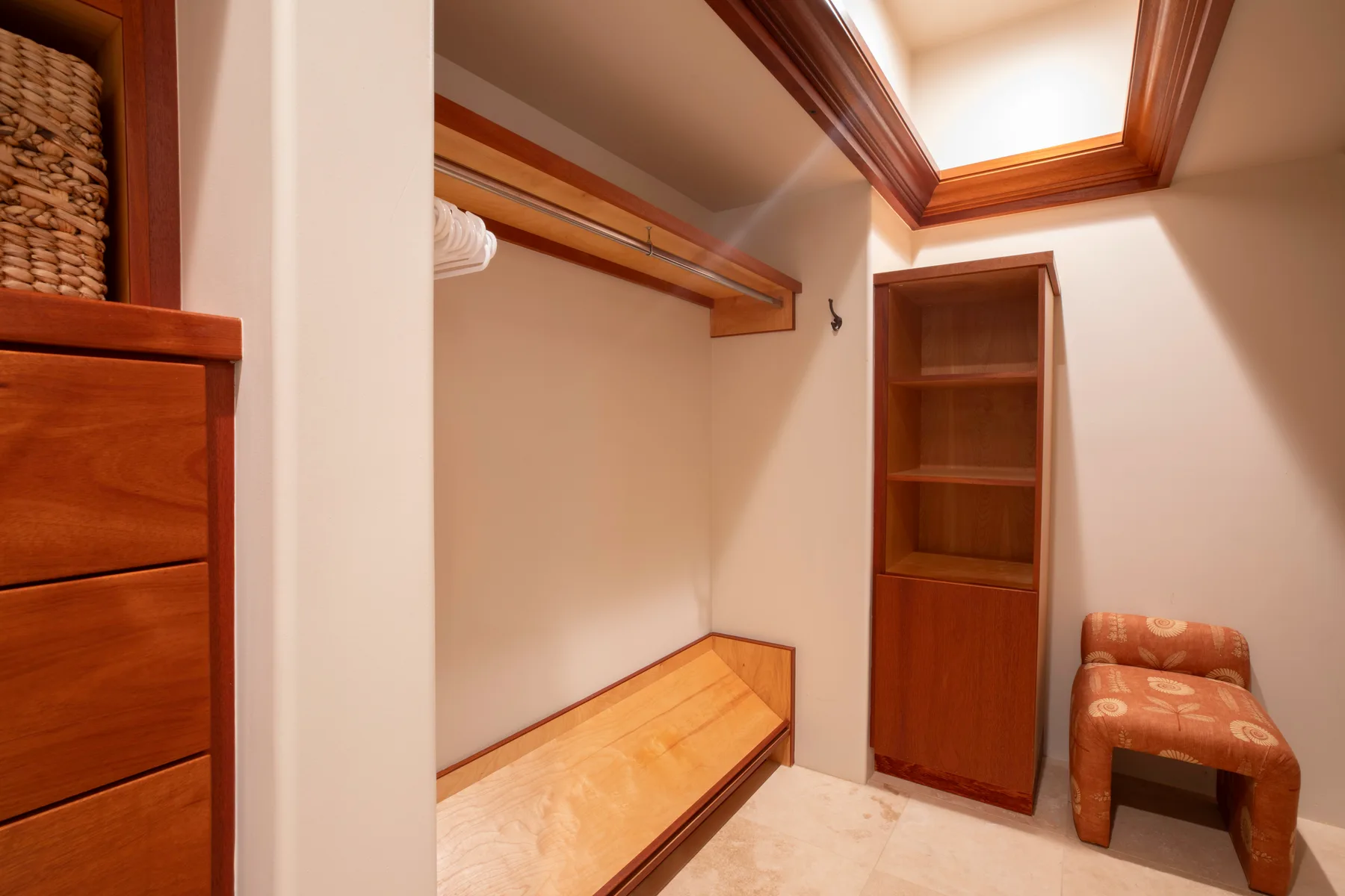 Un vestidor con estantes de madera, una barra para colgar ropa y un asiento acolchado.