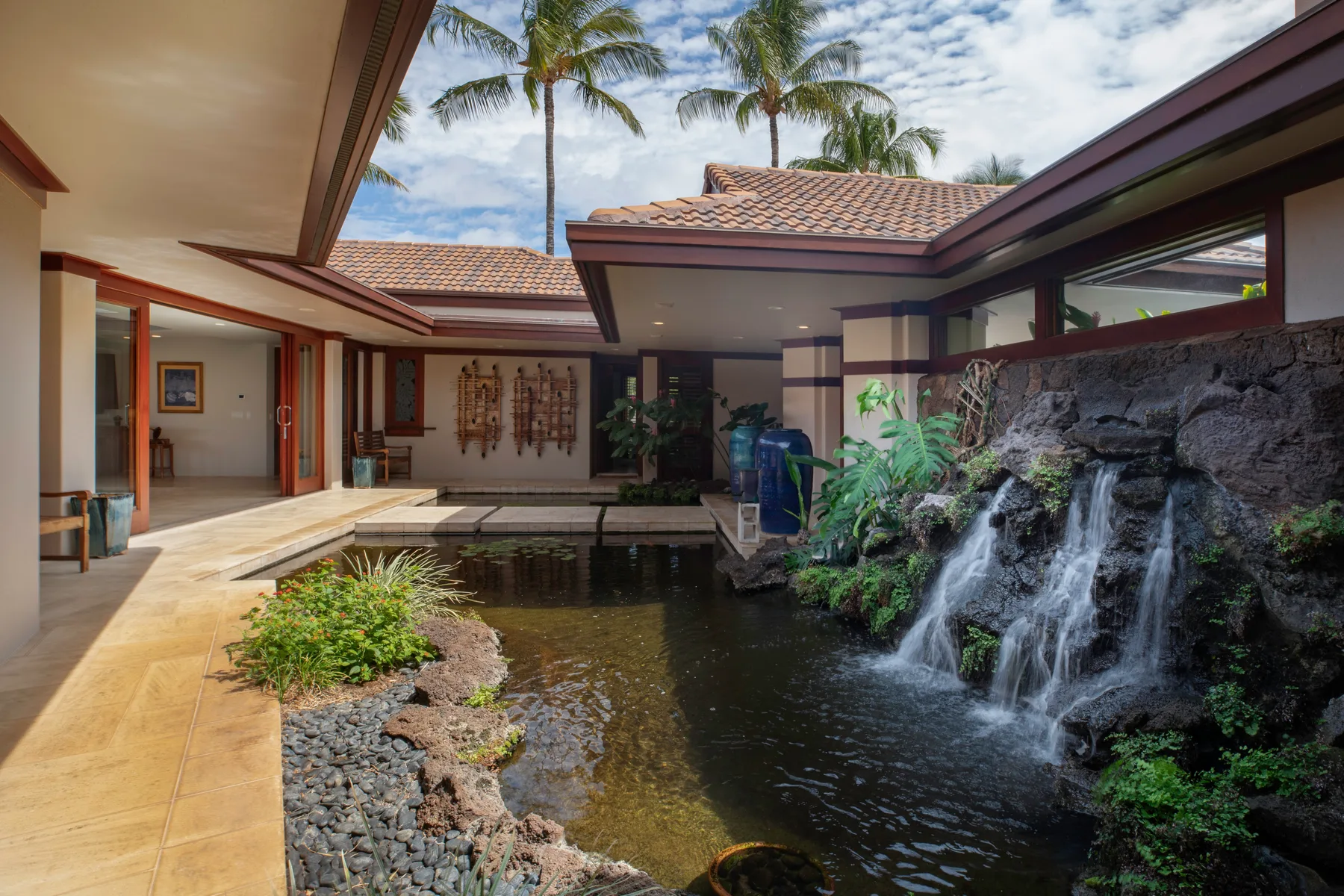 Un patio abierto rodea un estanque con una cascada y plantas tropicales.