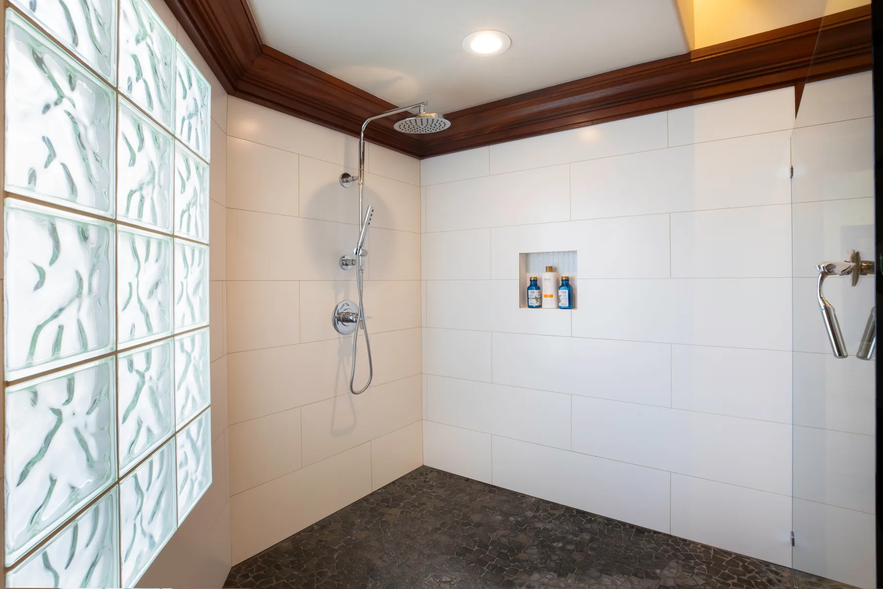 Área de ducha con paredes de azulejos, bloques de vidrio y ducha superior.