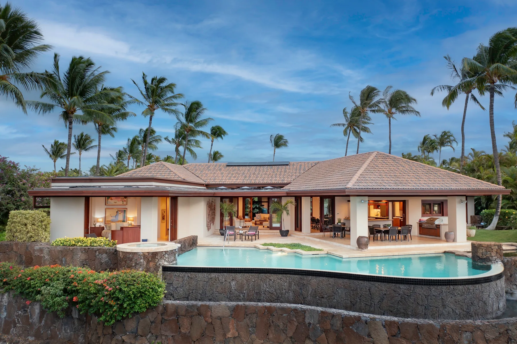 Una casa tropical da a una piscina curva, con palmeras detrás.