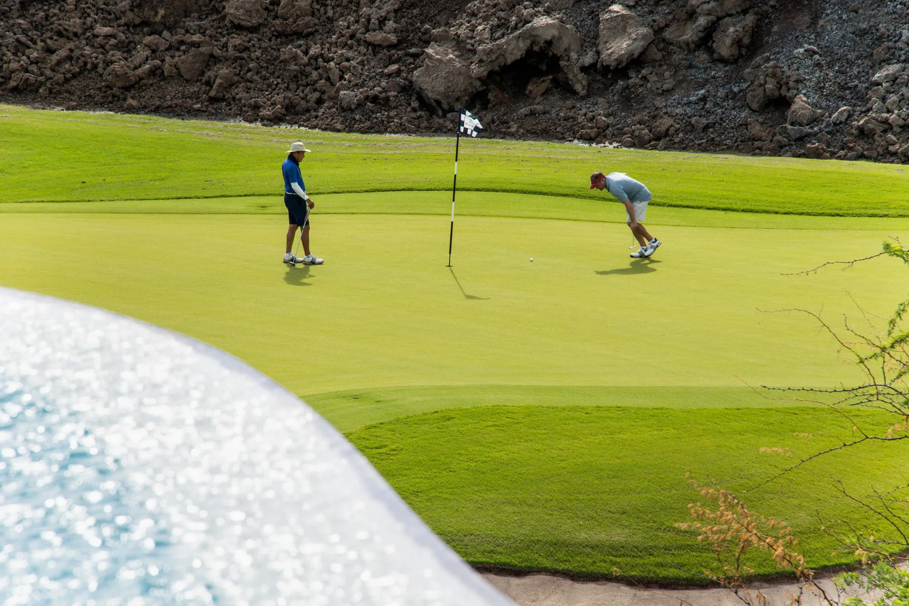Un green de golf con dos personas preparándose para patear cerca de la bandera.