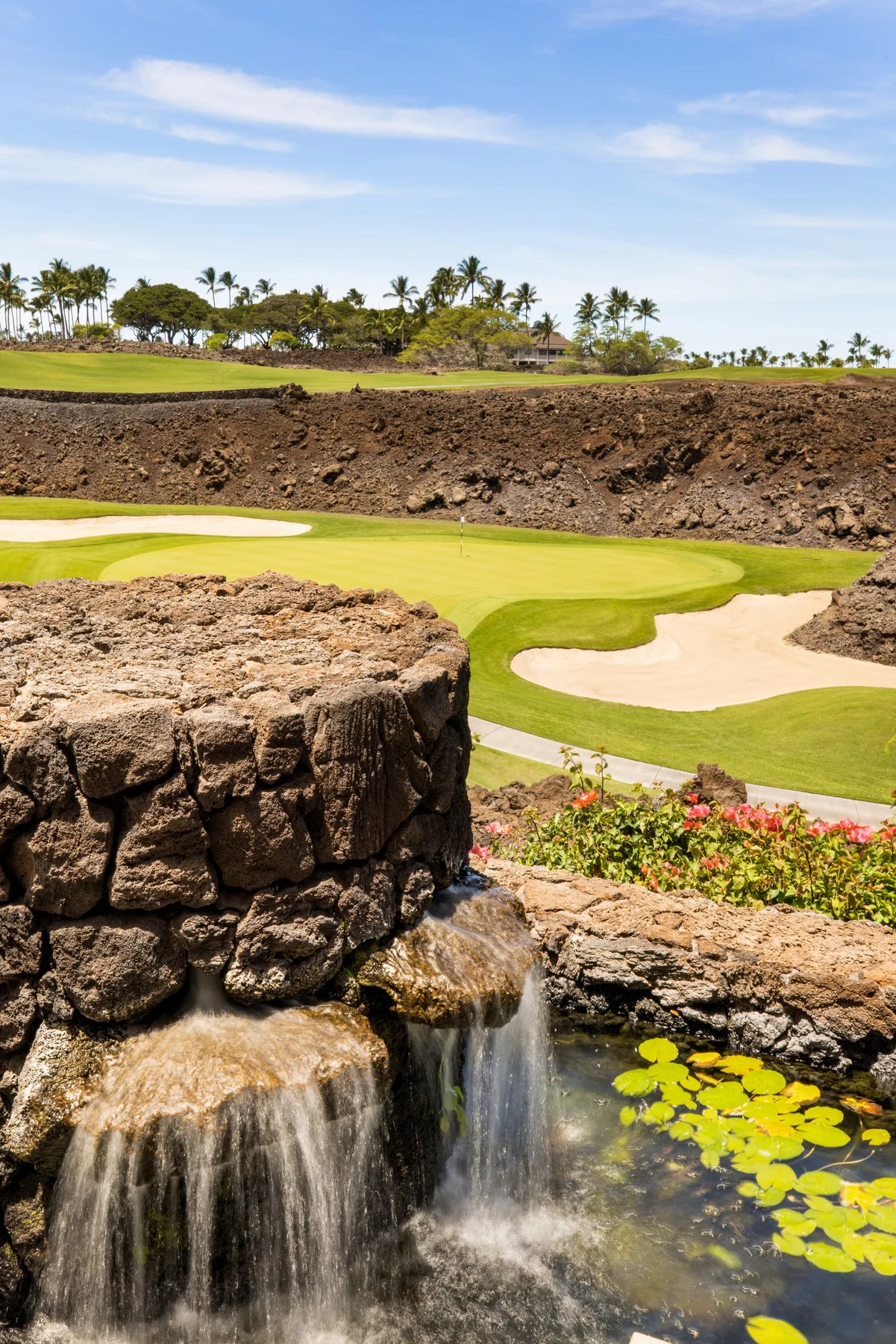 Un campo de golf con un búnker de arena queda detrás de una cascada rocosa y un estanque.