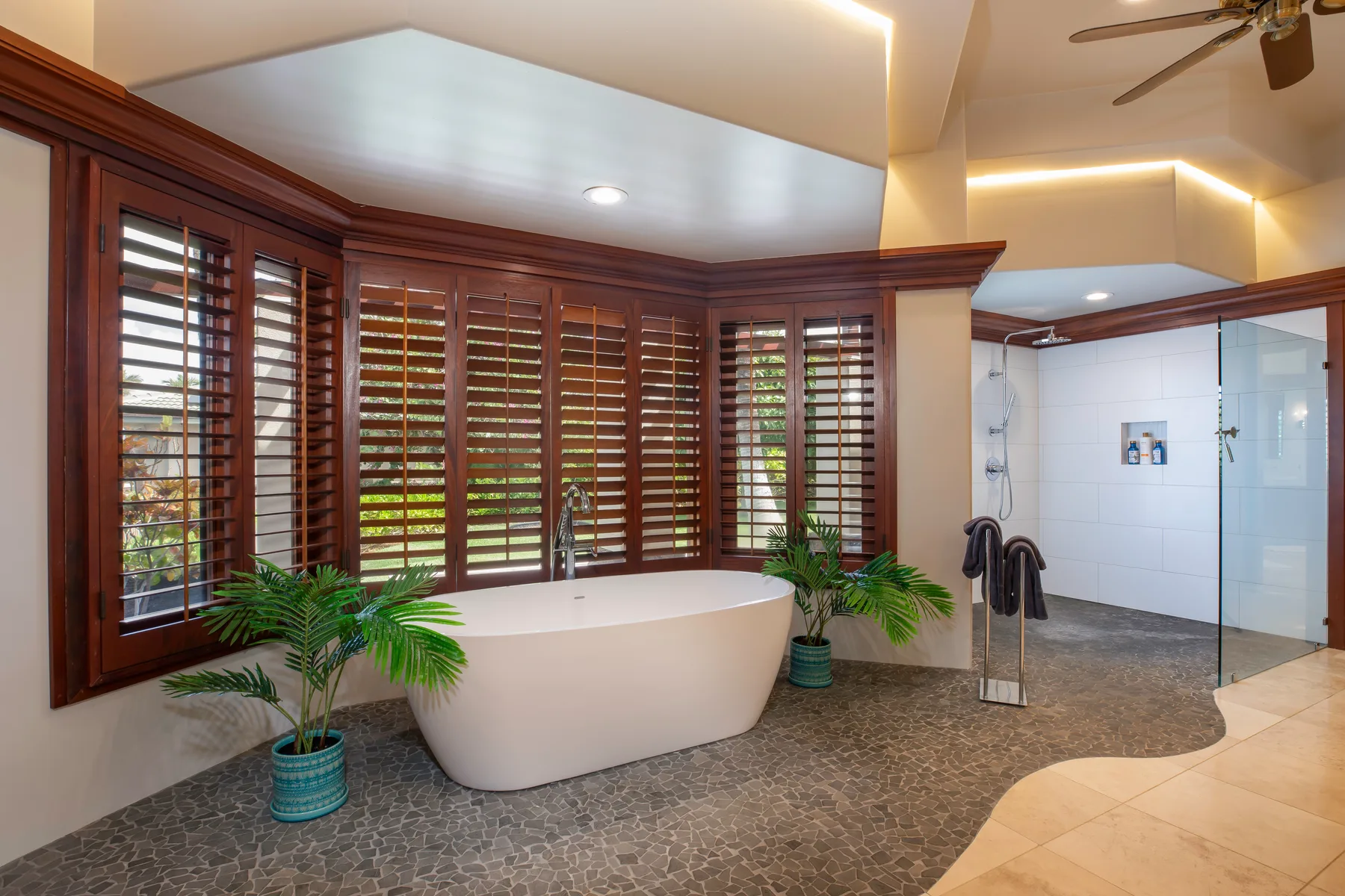 Un baño con una bañera exenta junto a ventanas con persianas y una zona de ducha.