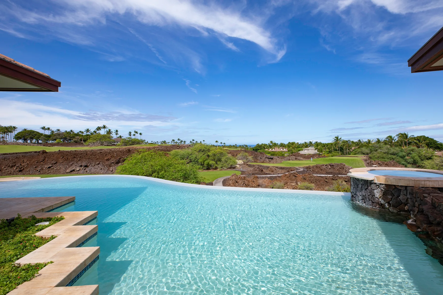 Una piscina al aire libre da a jardines bajo un cielo azul.