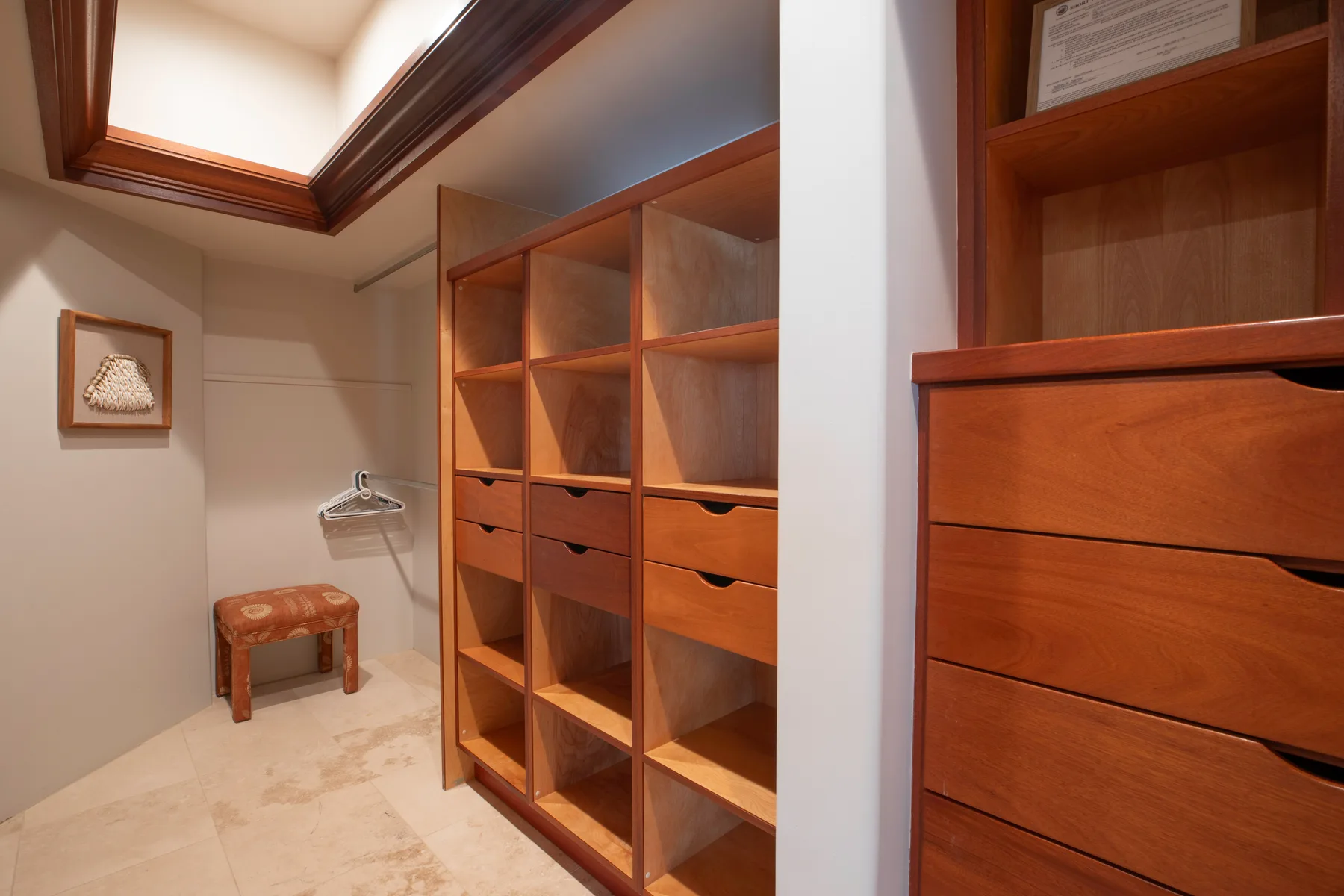 Un vestidor con estantes de madera abiertos, cajones y un pequeño taburete.