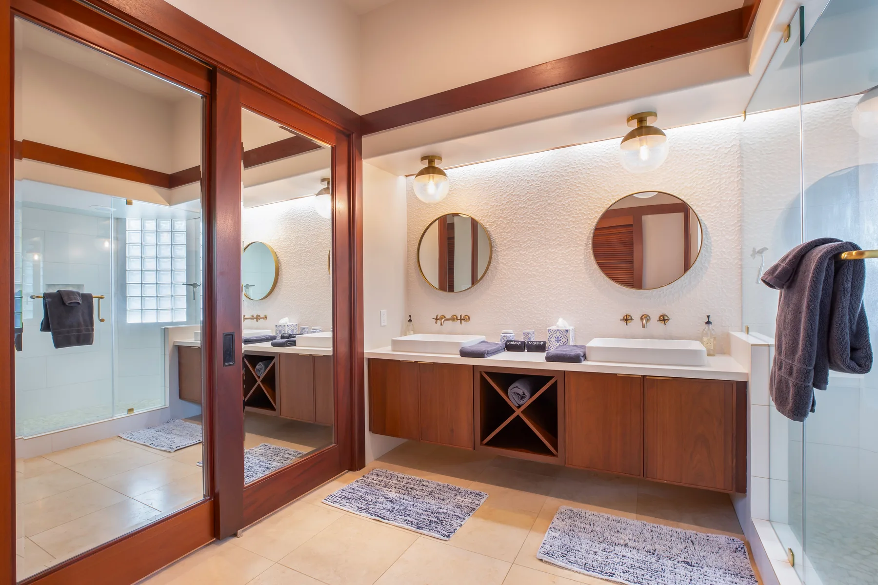 Un baño luminoso con dos lavabos, espejos redondos y mamparas de ducha de vidrio.