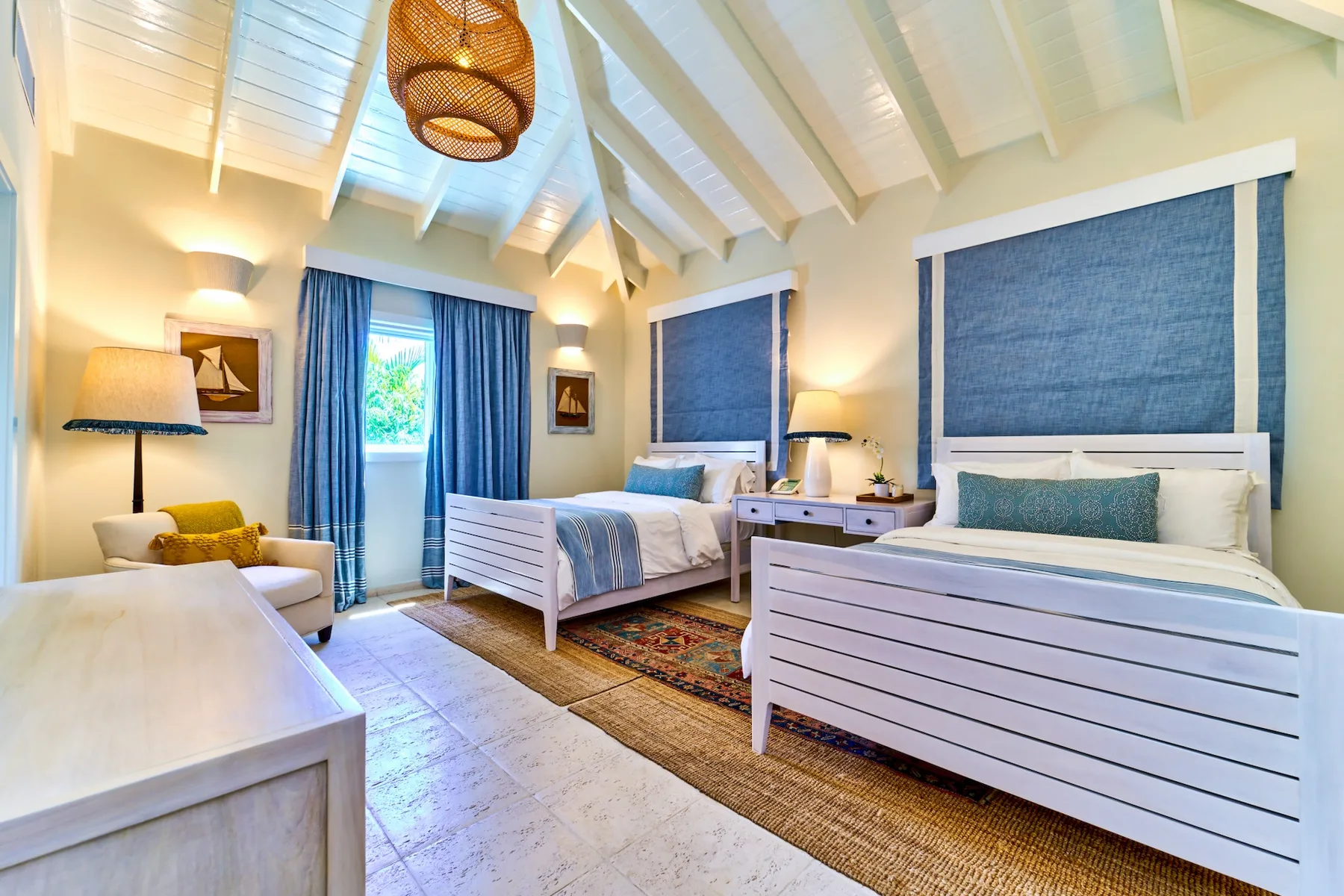 A bright bedroom with two beds, blue curtains, and a woven pendant light.