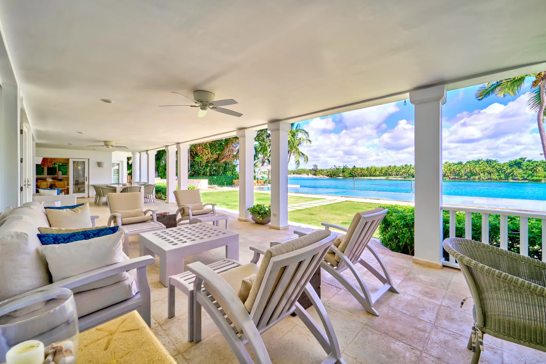 A covered patio with outdoor seating overlooks a pool and tropical greenery.