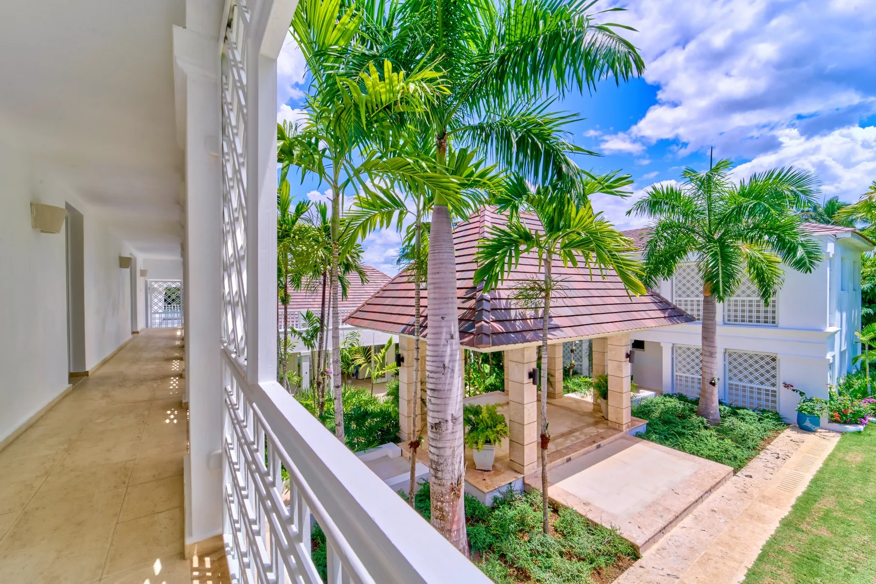 A covered walkway overlooks a landscaped courtyard with palm trees and a tiled pavilion.