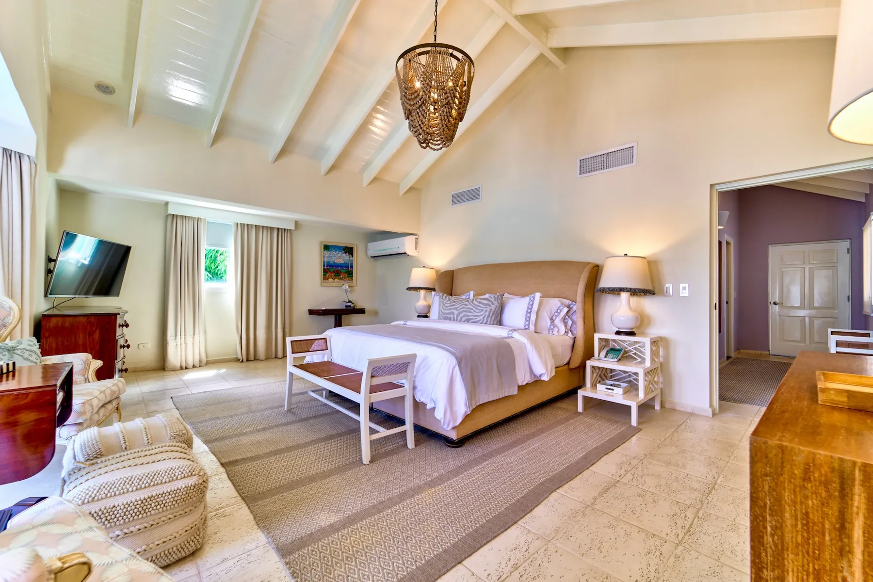 A bright bedroom with a large bed, exposed ceiling beams, and a sitting area.