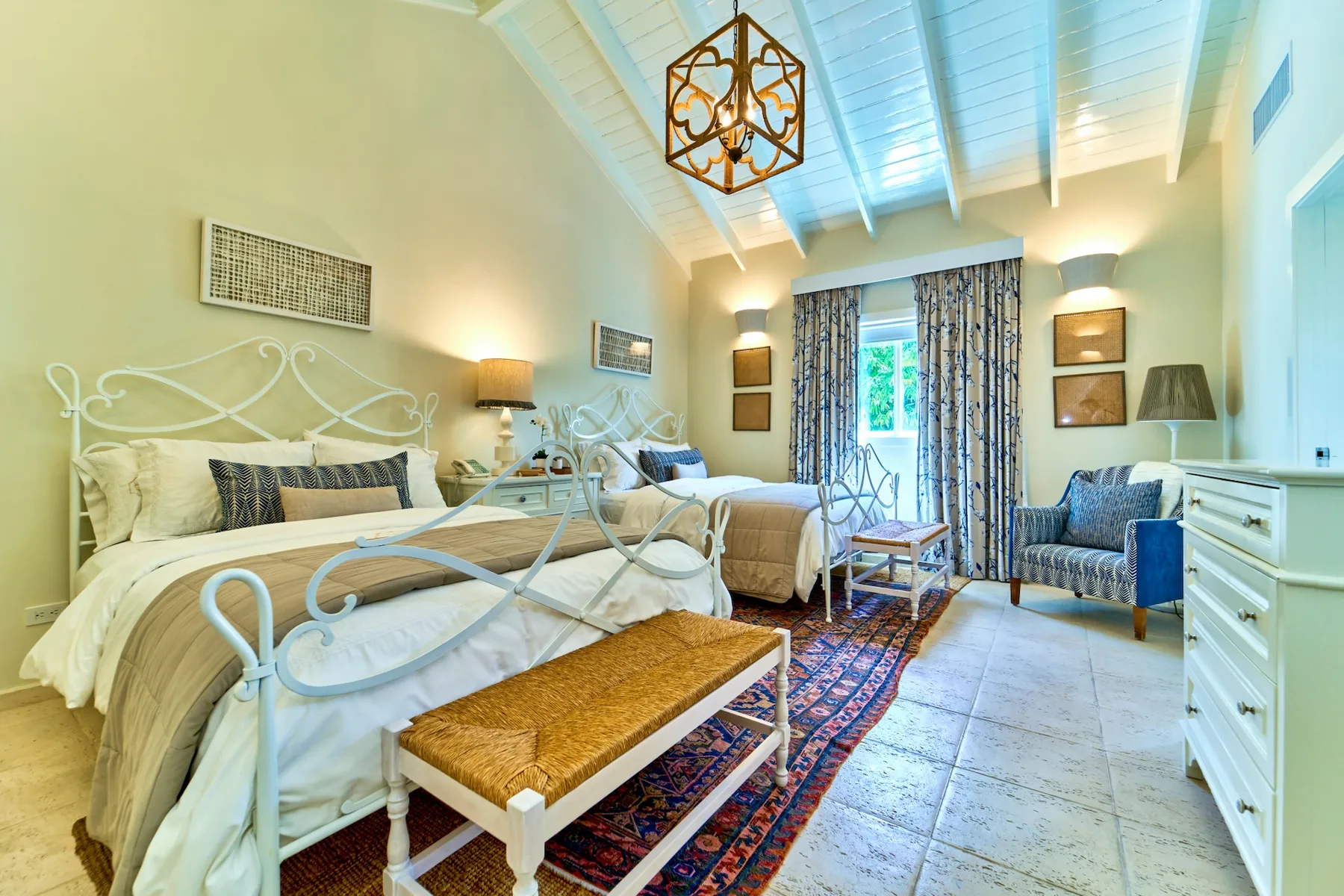A bright bedroom with two beds, a patterned rug, and a sitting area.