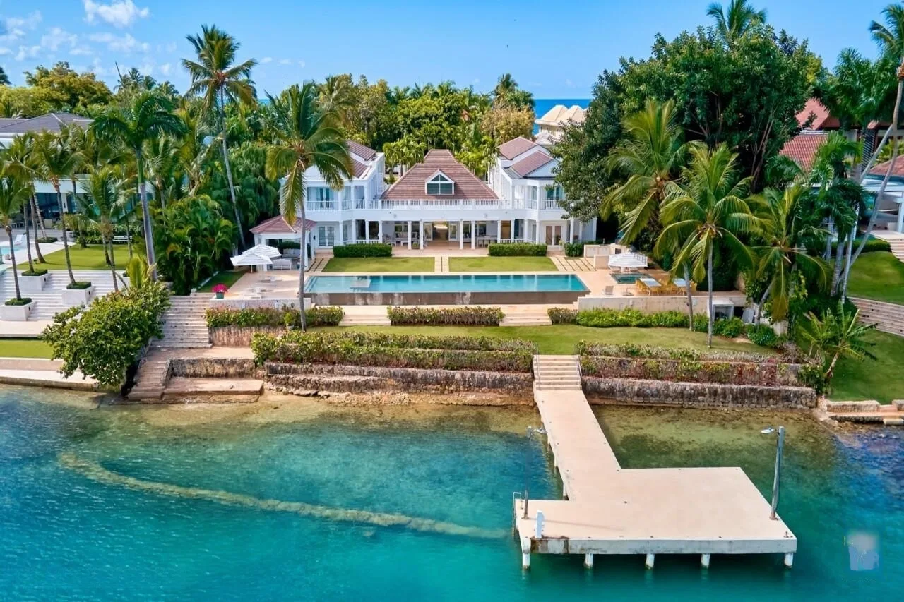 A waterfront villa and pool overlook clear turquoise water, with a pier extending from the shore.