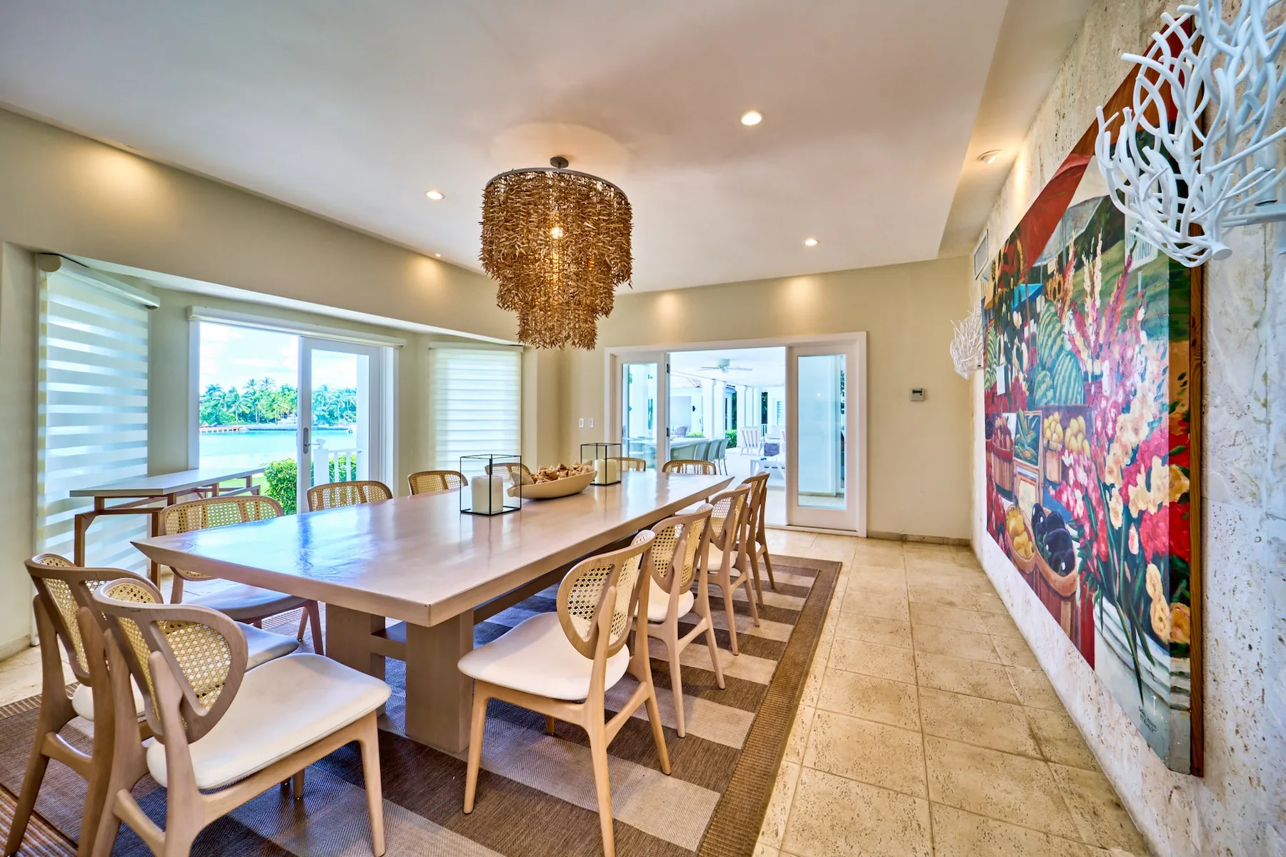 A dining area with a long table, woven chairs, and colorful wall art.