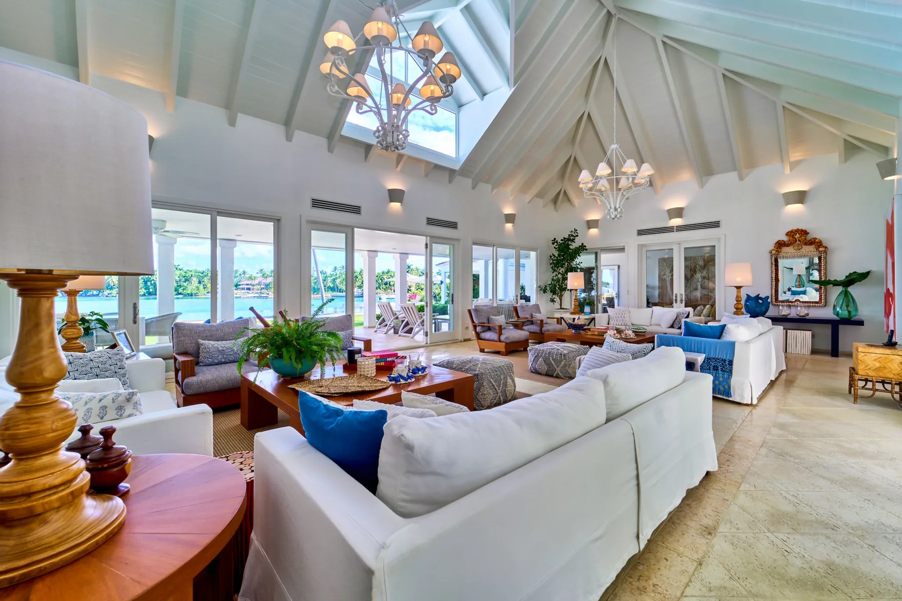 A bright living room with white seating and large windows opening onto greenery.