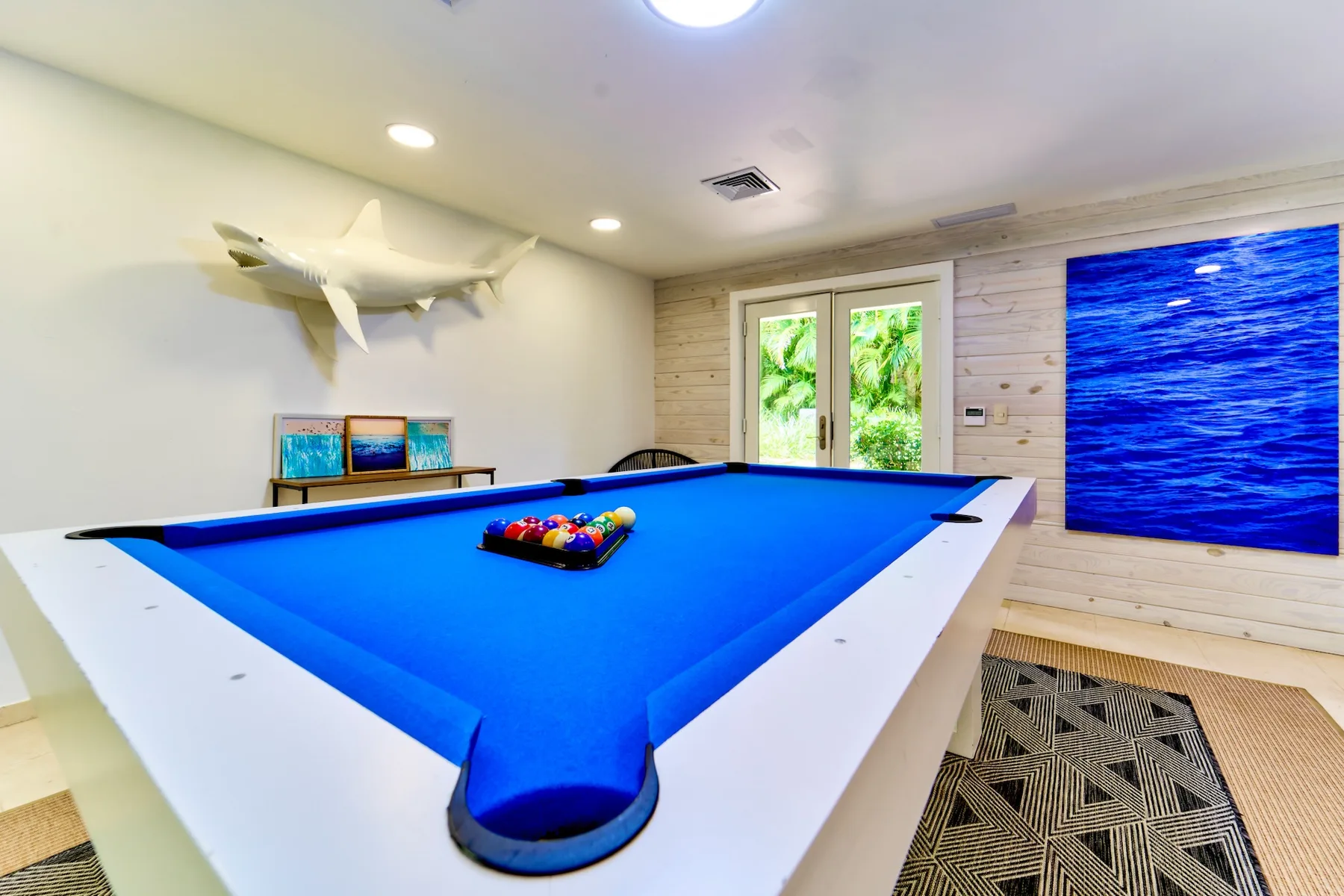 A game room with a blue-felt pool table and wall-mounted ocean artwork.