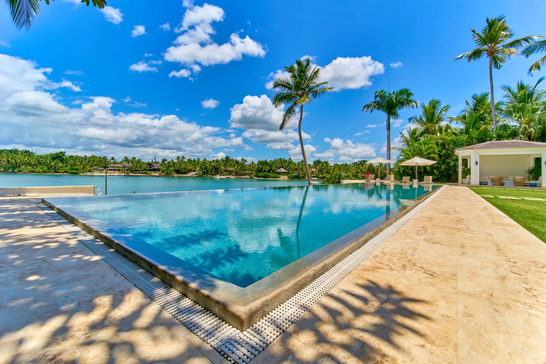An outdoor swimming pool sits beside a sandy-colored deck and tropical palms.