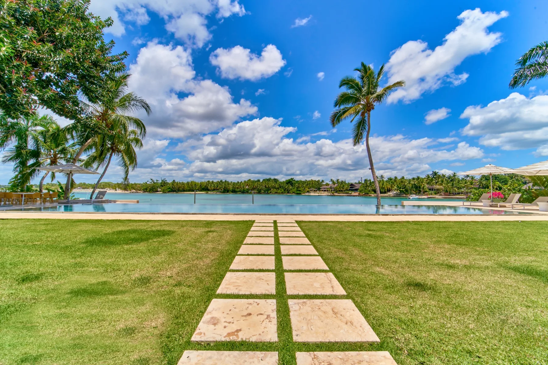 A grassy lawn and stepping-stone path lead toward a pool beneath a blue sky.