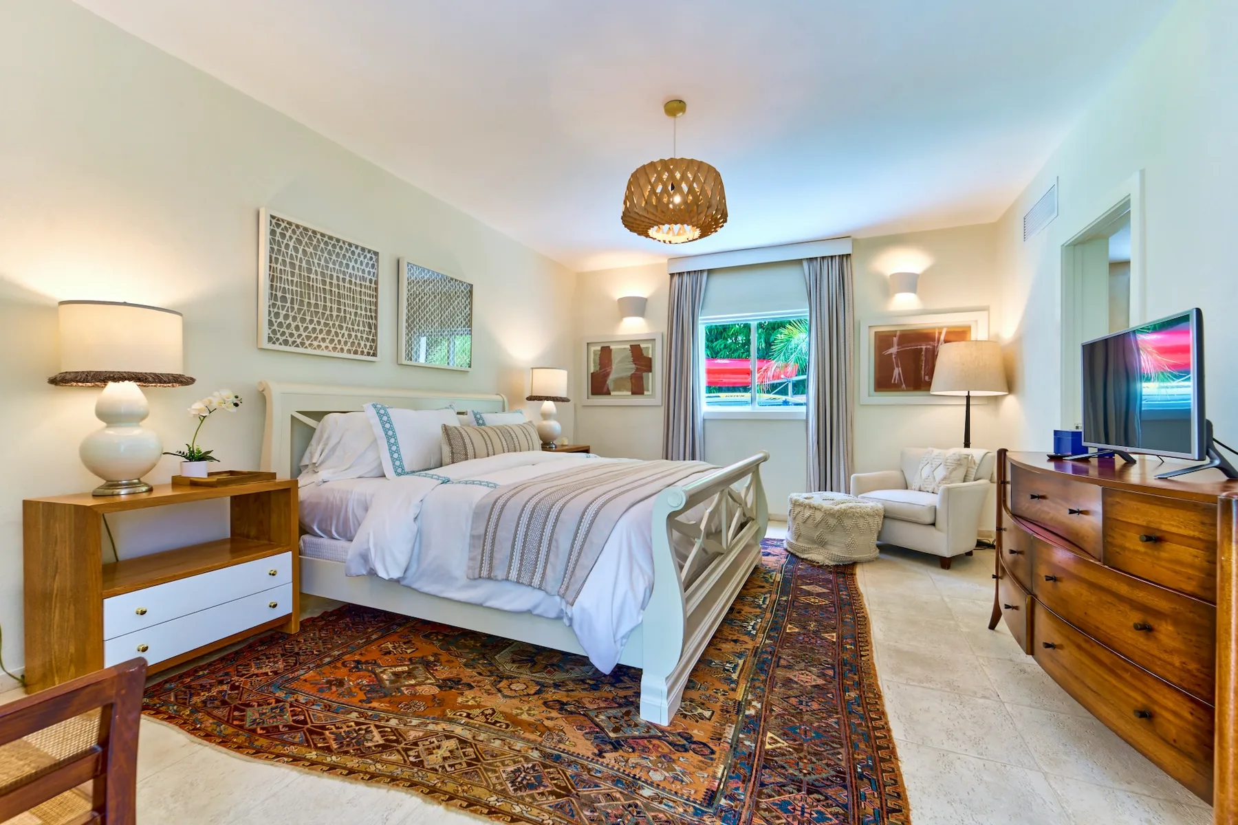 A bright bedroom with a large bed, patterned rug, and a window.