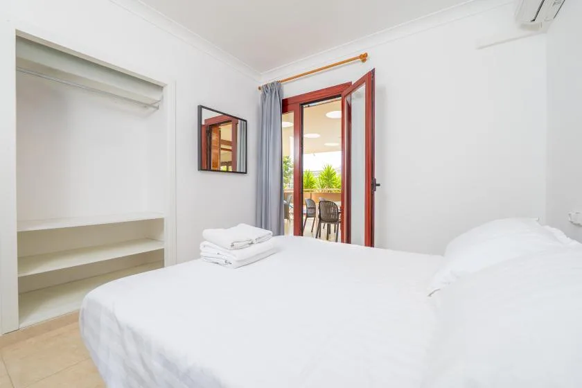 A bright bedroom with a white bed beside an open doorway to a balcony.