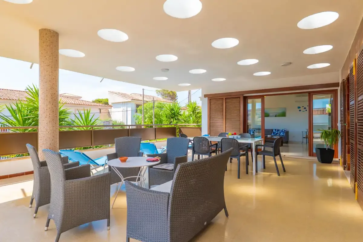 A covered outdoor dining area with tables and seating beside large windows.