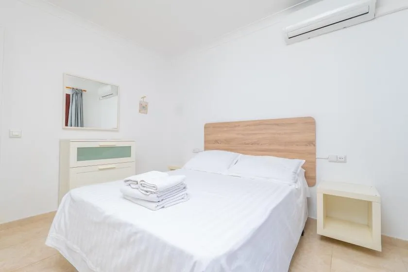 A bright bedroom with a double bed, white bedding, and a wooden headboard.