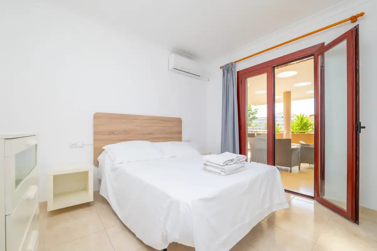 A bright bedroom with a white bed and sliding glass doors.