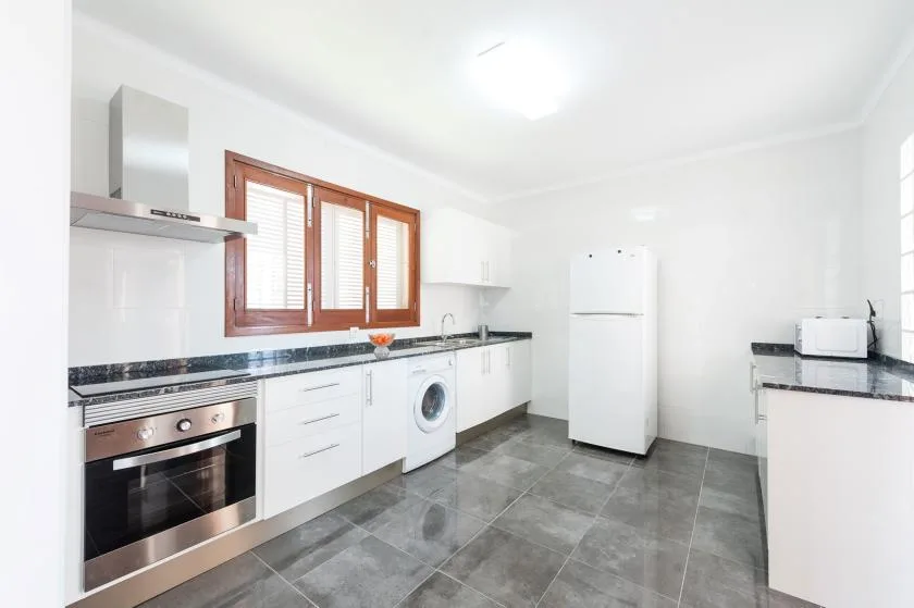A bright kitchen with white cabinets, dark countertops, and a large window.