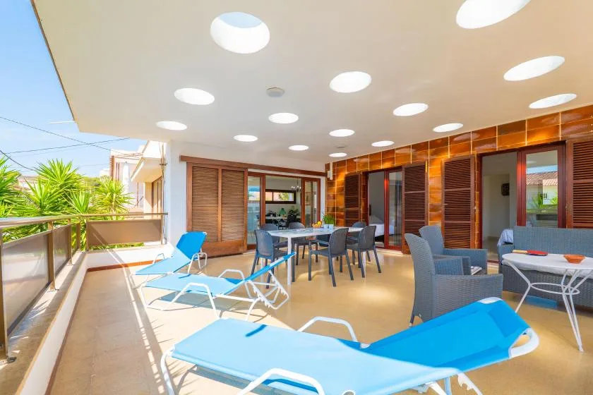 A bright outdoor patio with blue lounge seating beneath a covered roof.