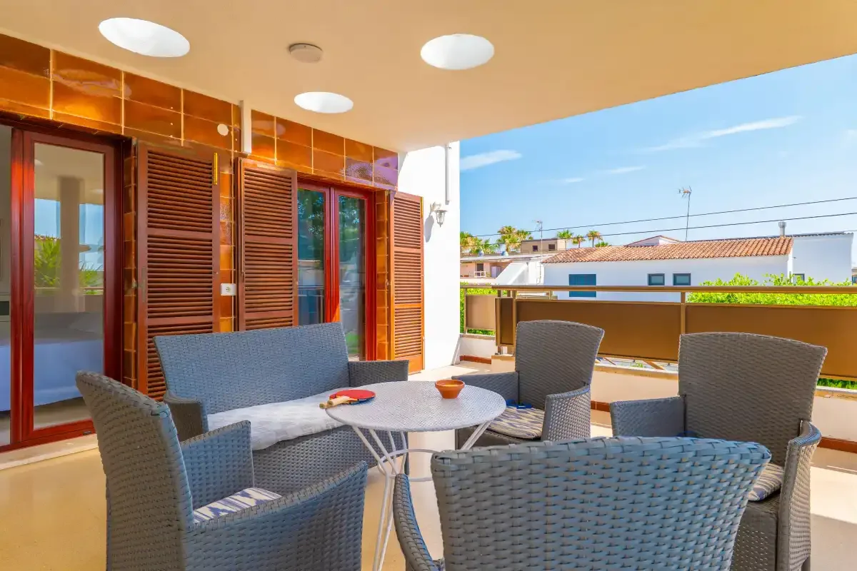 A sunny terrace with outdoor seating and a round table beside sliding glass doors.