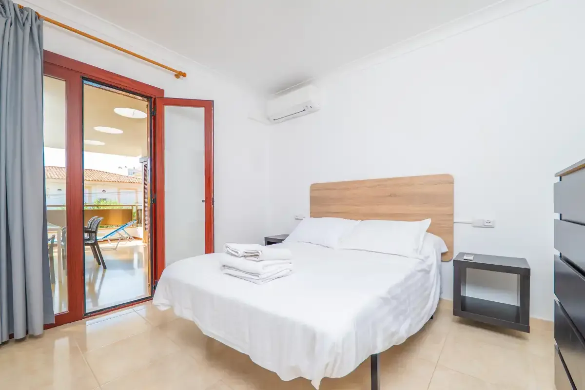 A bright bedroom with a neatly made bed and glass doors opening onto a balcony.