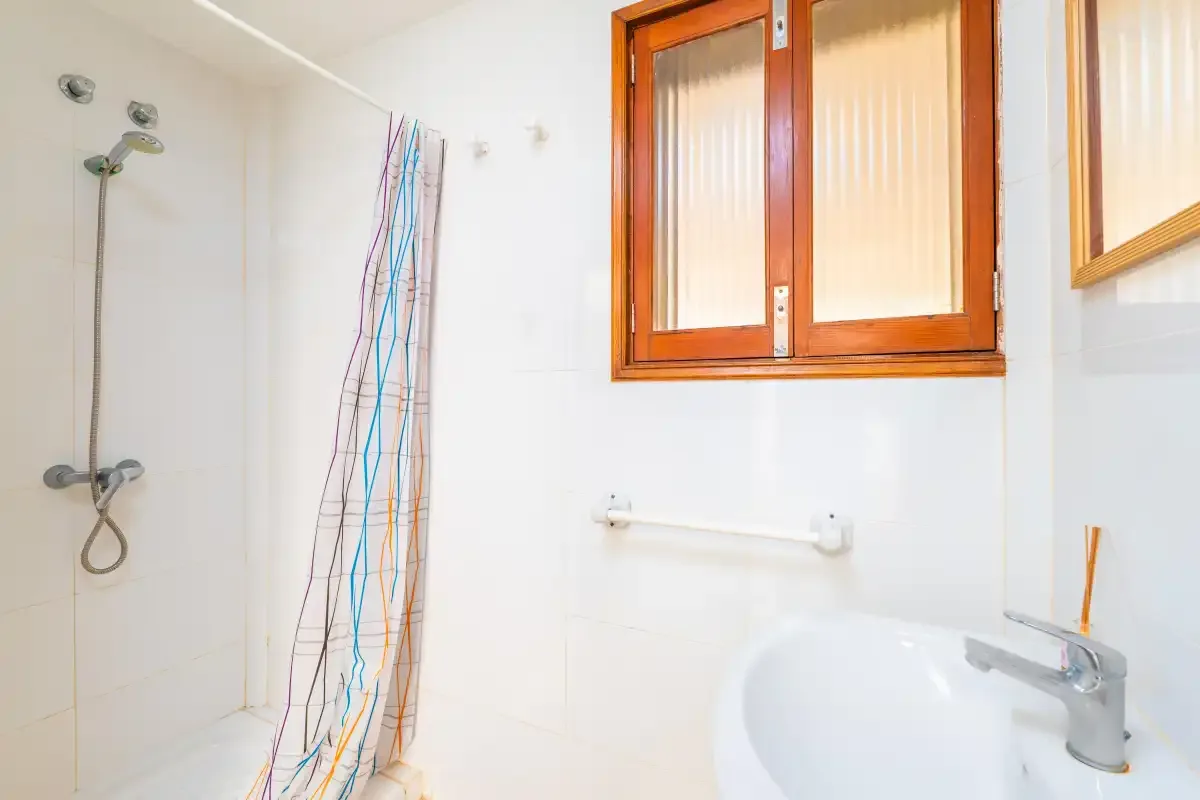 A tiled bathroom with a shower, sink, and wooden-framed window.