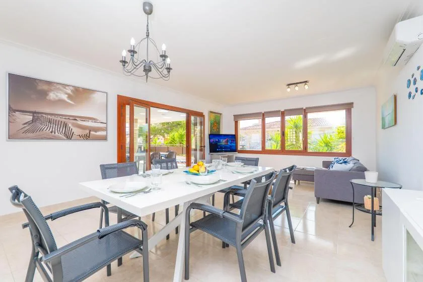 A bright dining and living area with a long table and seating beside large windows.