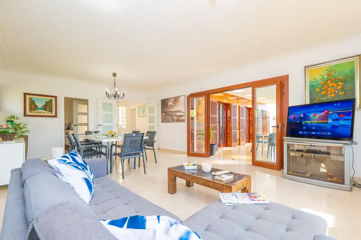 A bright living and dining area with seating, a television, and open glass doors.