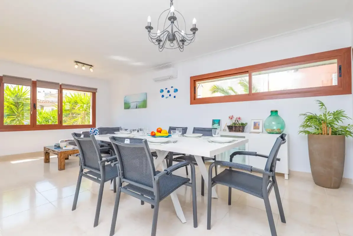 A bright dining area with a long table, seating, and large windows.