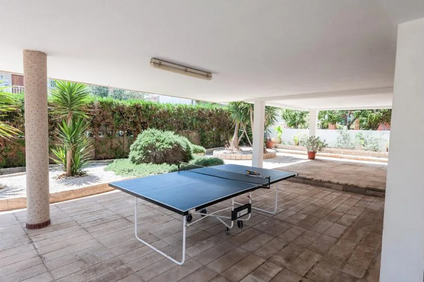 A covered patio has a ping-pong table beside a planted garden.