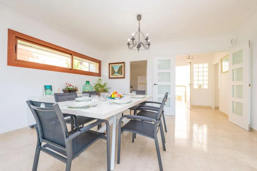 A bright dining room with a set table and chairs beneath a chandelier.