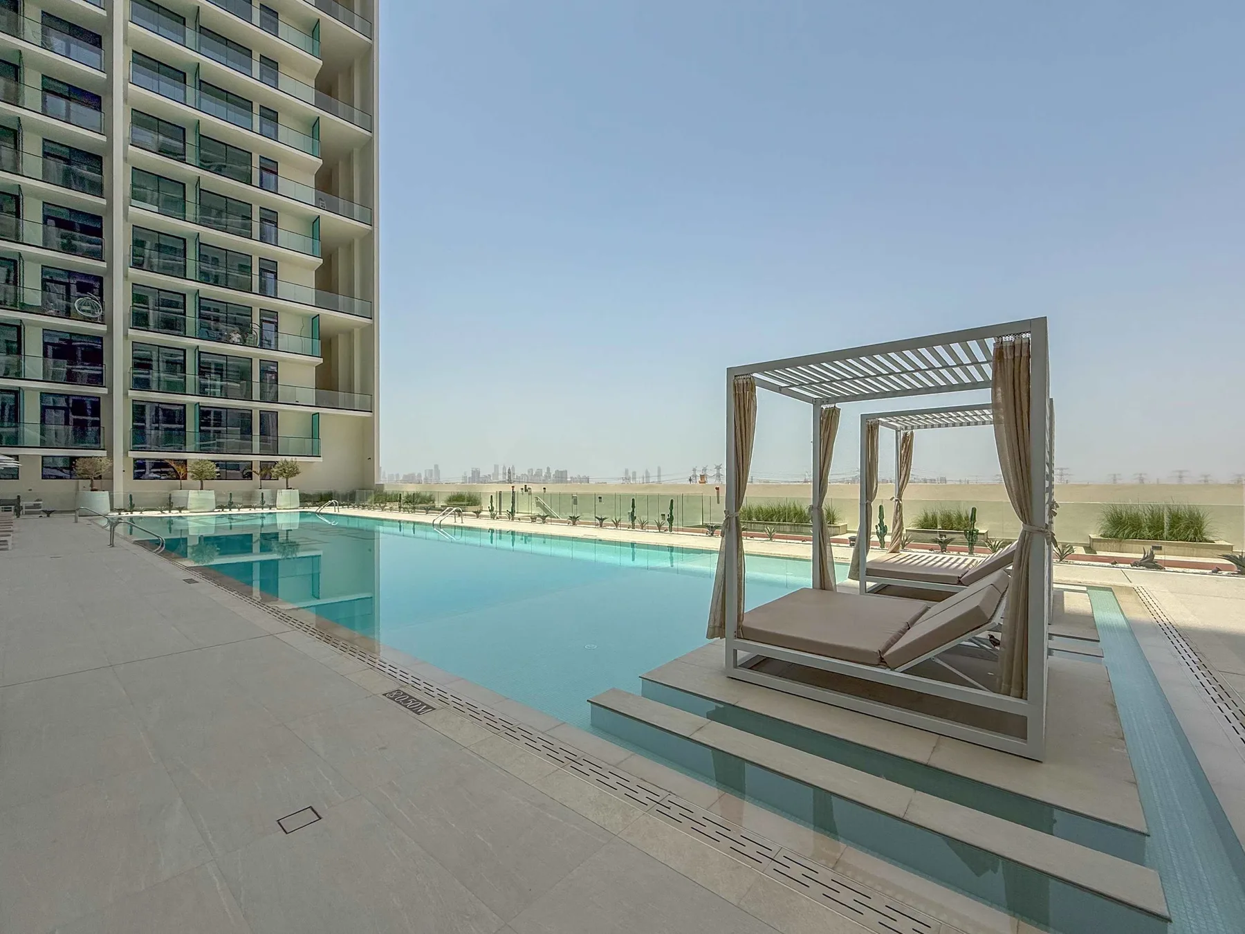 An outdoor swimming pool beside a modern building, with shaded lounge seating.