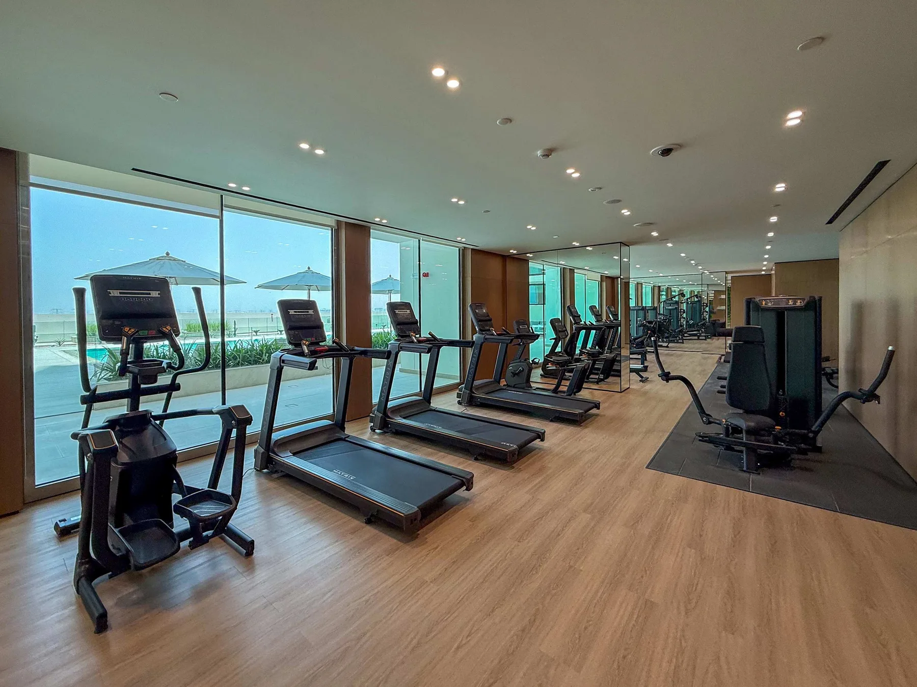 A gym with rows of exercise machines beside large windows.