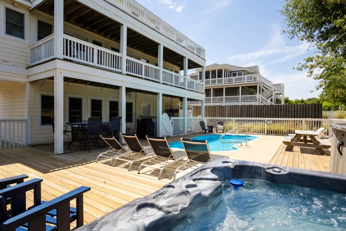Una piscina exterior y un jacuzzi están junto a un edificio de varios pisos con terrazas de madera.