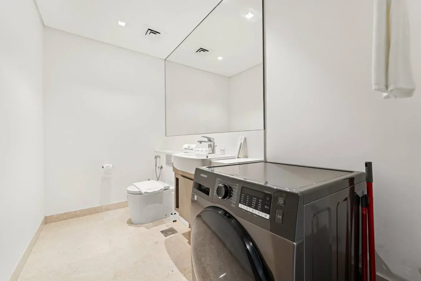 Una zona luminosa de lavandería y baño tiene una lavadora junto al lavabo y al inodoro.
