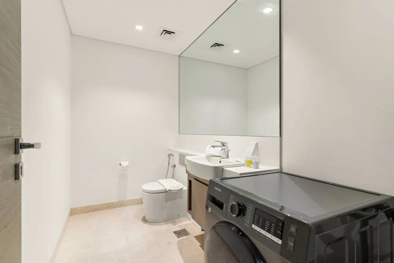Un baño con lavabo, inodoro y lavadora de carga frontal.