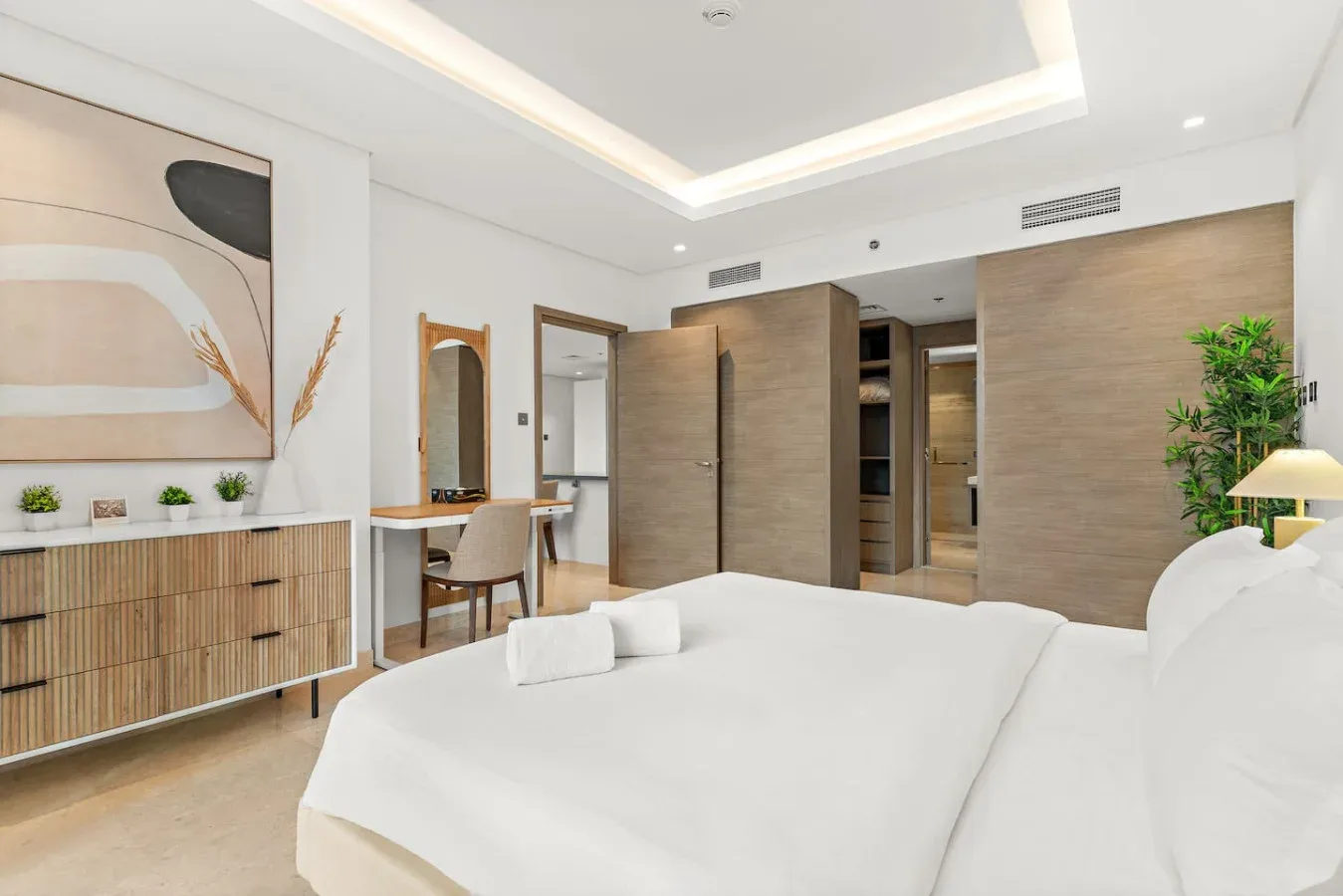 Un dormitorio luminoso con una cama grande, un escritorio y un cuadro abstracto.