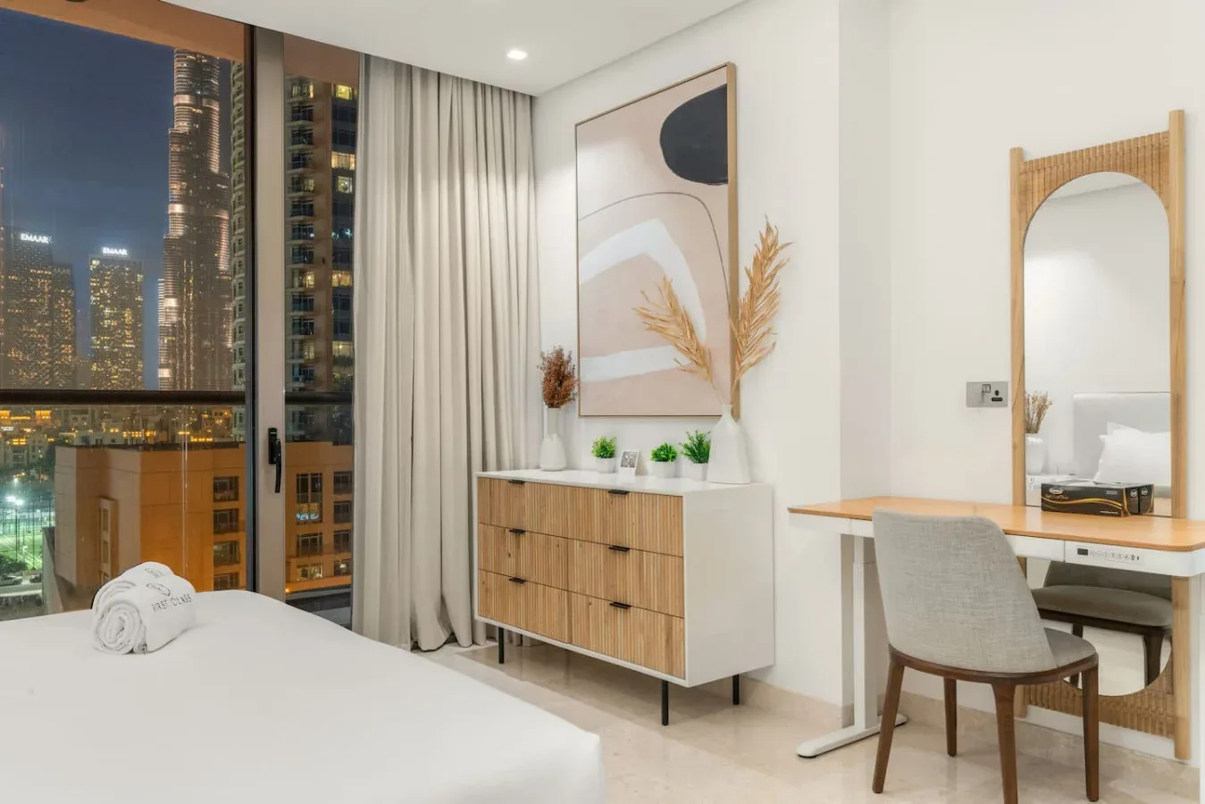 Un dormitorio luminoso con cama, cómoda y escritorio junto a una ventana grande.