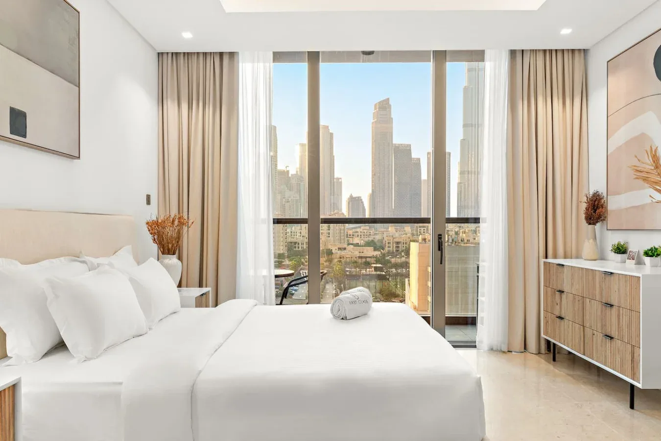 Un dormitorio luminoso con una cama junto a ventanales con vistas a edificios de la ciudad.
