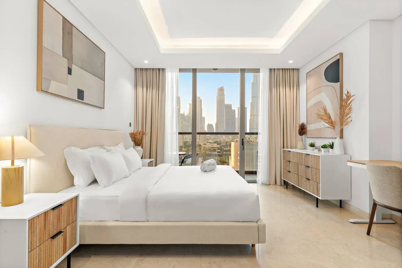Un dormitorio luminoso con una cama grande frente a ventanales con vistas a la ciudad.