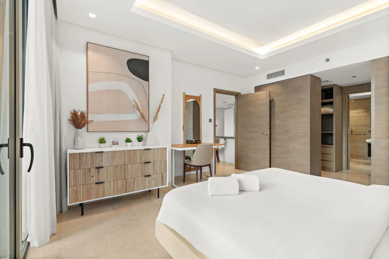 Un dormitorio luminoso con una cama bien tendida y un escritorio junto al armario.