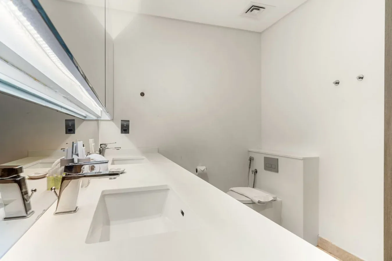 Un baño luminoso con una encimera blanca larga y un lavabo integrado.