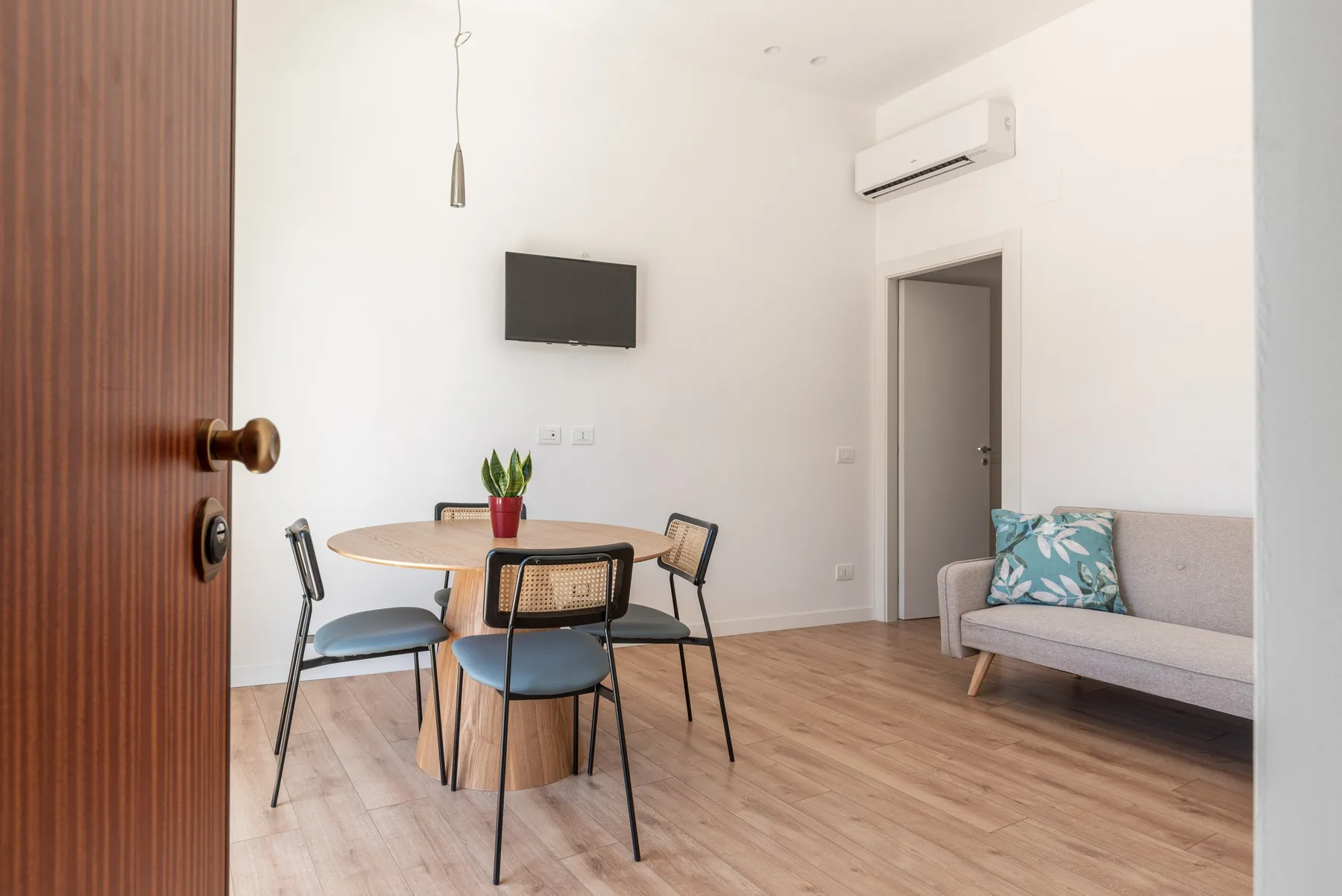 Una luminosa sala de estar y comedor con mesa, asientos y un televisor en la pared.
